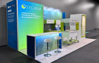 large exhibition stand with blue and green walls at the back. A lit counter with two stools and some chemical equipment are set in front of the rear wall
